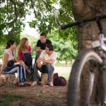 En gruppe unge mennesker hygger i parken - cykel parkeret op ad et træ